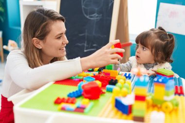 Teacher and toddler playing with construction blocks sitting on table at kindergarten