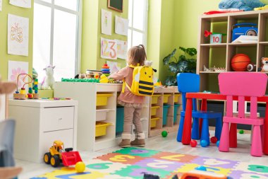 Adorable blonde girl wearing backpack standing at kindergarten