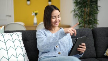 Evdeki kanepede oturan dokunmatik ped kullanan genç ve güzel İspanyol kadın.