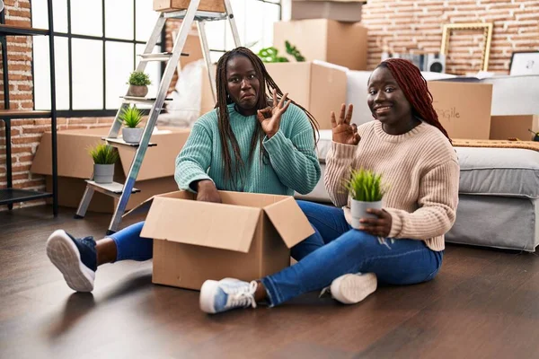 Two African Woman Moving New Home Sitting Floor Doing Sign — Stock Photo, Image