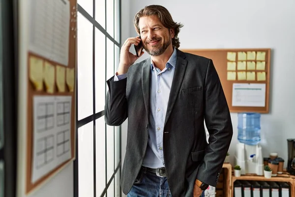 中年Cucasian男笑顔自信を持って話して上のスマートフォンでオフィス — ストック写真