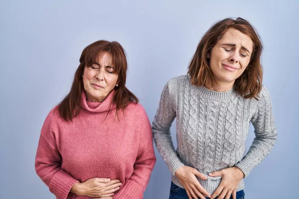 母亲和女儿站在蓝色的背景上 双手放在肚子上 因为消化不良 痛苦不堪 疼痛的概念 — 图库照片
