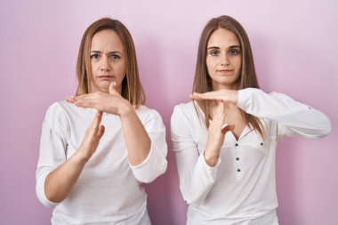 Orta yaşlı anne ve küçük kızı pembe arka planda duruyor. Elleriyle jest yapıyor, hayal kırıklığına uğramış ve ciddi bir yüz ifadesi takınıyor. 
