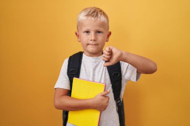 Küçük beyaz çocuk öğrenci çantası takıyor ve elinde kızgın suratlı bir kitap tutuyor. Negatif işaret baş parmakları aşağıda, reddedilme konsepti ise... 