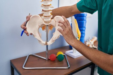 Young caucasian man physiotherapist touching anatomical model of spinal column at rehab clinic