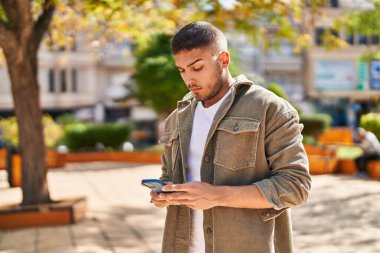 Young hispanic man using smartphone at park