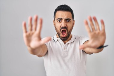 Young hispanic man with beard wearing casual clothes over white background doing stop gesture with hands palms, angry and frustration expression 