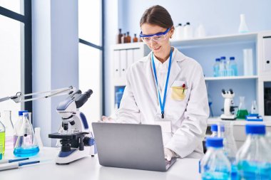 Young caucasian woman scientist smiling confident using laptop at laboratory
