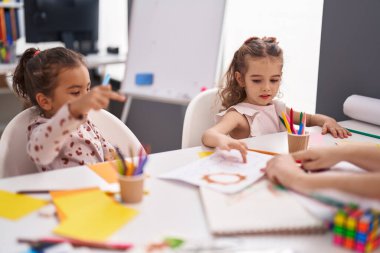İki çocuk anaokulu öğrencisi sınıfta öğretmenden ders alıyorlar.