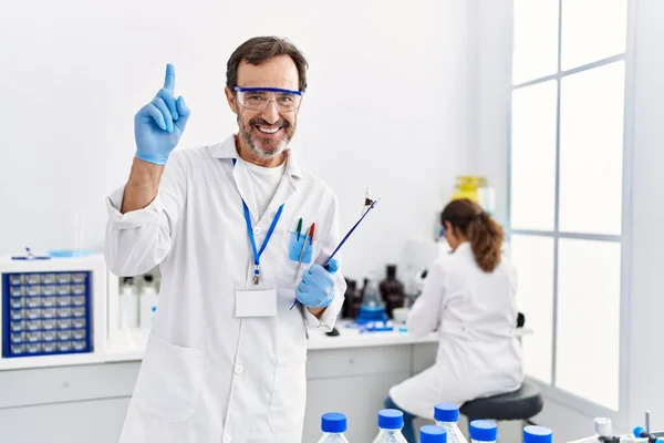 Middle age man working at scientist laboratory surprised with an idea or question pointing finger with happy face, number one