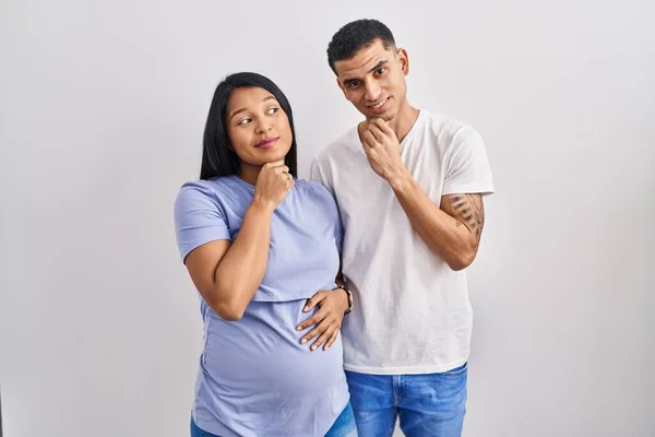 Young Hispanic Couple Expecting Baby Standing Background Hand Chin Thinking — ストック写真