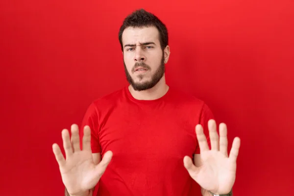 カジュアルな赤いTシャツを着た若いヒスパニック系の男性は 恐怖と嫌な表情で拒否と否定を示す手のひらを離れて移動します 止めて禁止する — ストック写真