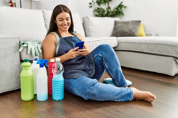 Young Beautiful Hispanic Woman Using Smartphone Sitting Floor Clean Products — ストック写真