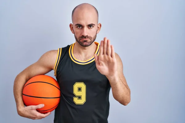 年轻的秃头男子 留着胡子 身穿篮球服 手心紧握球 停止歌唱 用消极而严肃的手势警告人 — 图库照片