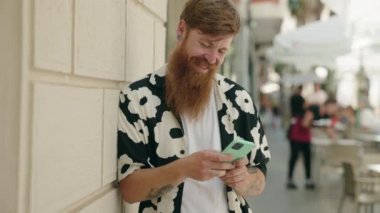 Young redhead man smiling confident using smartphone at street