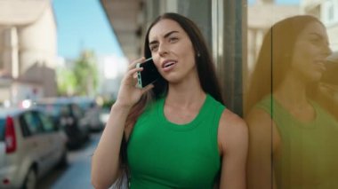 Genç, güzel, İspanyol bir kadın gülümsüyor ve caddede akıllı telefondan konuşuyor.
