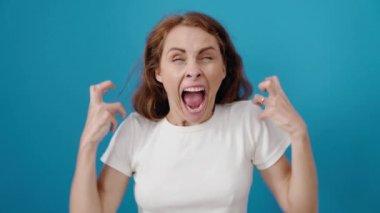 Güzel İspanyol bir kadın öfkeli bir ifadeyle, izole edilmiş mavi arka planda duruyor.