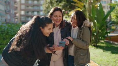 Mother and daughters smiling confident using smartphone at park