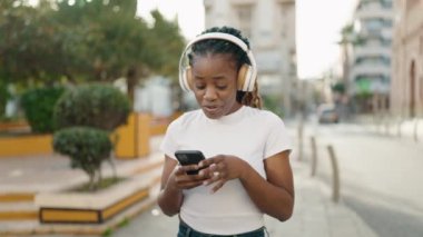 Afro-Amerikalı kadın parkta akıllı telefon kullanarak gülümsüyor.