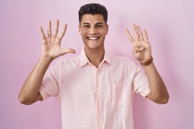 Young hispanic man standing over pink background showing and pointing up with fingers number nine while smiling confident and happy. 