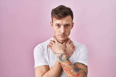Caucasian man standing over pink background shouting suffocate because painful strangle. health problem. asphyxiate and suicide concept. 