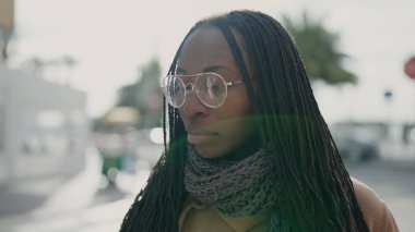 African woman standing with serious expression wearing glasses at street