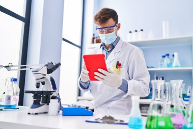 Young man scientist wearing medical mask using touchpad at laboratory