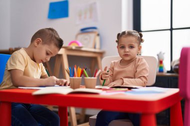 Anaokulunda iki anaokulu öğrencisi masaya oturmuş kağıda resim çiziyor.