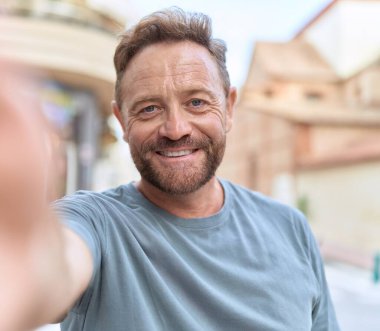 Middle age man smiling confident making selfie by camera at street