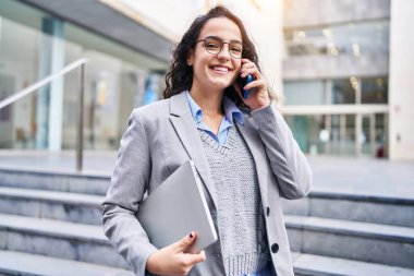 Genç İspanyol kadın yönetici caddede akıllı telefondan konuşuyor.