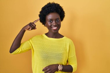 African young woman standing over yellow studio smiling pointing to head with one finger, great idea or thought, good memory 