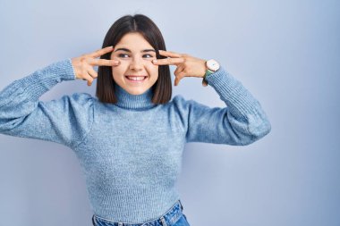 Mavi arka planda dikilen genç İspanyol kadın barış sembolü yapıyor. Yüzünde parmakları, gülümseyerek zaferi gösteriyor. 