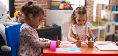 Two kids preschool students sitting on table drawing on paper at kindergarten