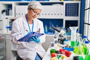 Middle age woman wearing scientist uniform writing on document at laboratory