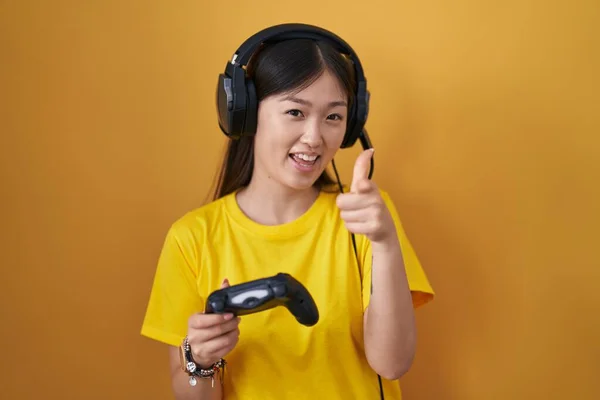 中国的年轻女子正在玩电子游戏 手里拿着控制器 手指着相机 脸上洋溢着欢乐和滑稽的表情 充沛的精力和活力 — 图库照片