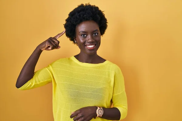 一本の指で頭を指して笑顔黄色のスタジオの上に立ってアフリカの若い女性 素晴らしいアイデアや考え 良い記憶 — ストック写真