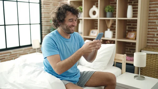 Young Hispanic Man Using Smartphone Sitting Bed Bedroom — Stok fotoğraf