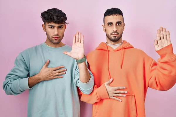 Young Hispanic Gay Couple Standing Pink Background Swearing Hand Chest — Fotografia de Stock
