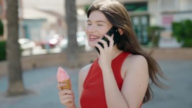 Beyaz bir kadın akıllı telefondan konuşuyor. Parkta dondurma yiyor.