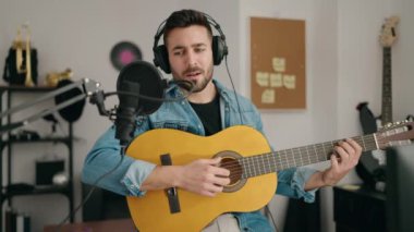 Genç İspanyol bir adam müzik stüdyosunda klasik gitar çalarak şarkı söylüyor.
