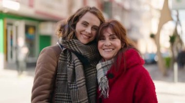 Mother and daughter hugging each other doing heart gesture with hands at street