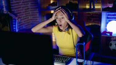Young african american woman streamer playing video game with surprise expression at gaming room