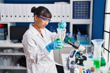 Genç ve güzel İspanyol bilim kadını laboratuarda test tüpüne sıvı döküyor.