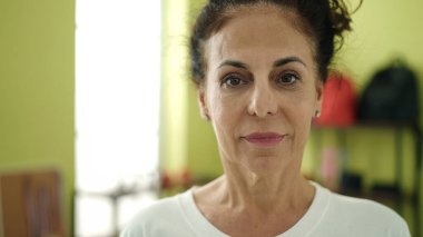 Middle age hispanic woman standing with relaxed expression at sport center