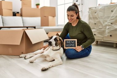 Genç bir kadın köpeğiyle yerde oturuyor ve elinde evde yeni bir karatahta mesajı var.