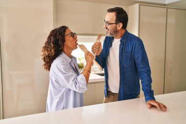 Orta yaşlı İspanyol çift, mutfakta şarkı söylerken gülümsüyor.