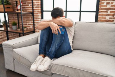 Young hispanic man stressed sitting on sofa at home