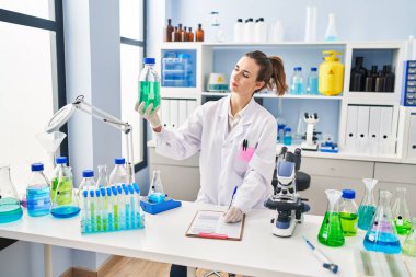 Laboratuvarda elinde şişe tutarken bilim adamı üniforması giyen genç bir kadın.