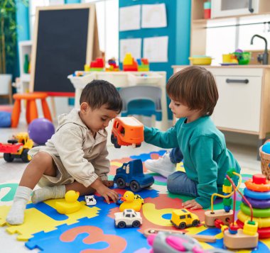 Two kids playing with cars toy sitting on floor at kindergarten