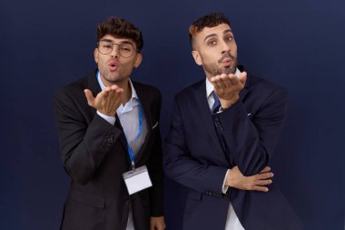 Two hispanic business men wearing business clothes looking at the camera blowing a kiss with hand on air being lovely and sexy. love expression. 